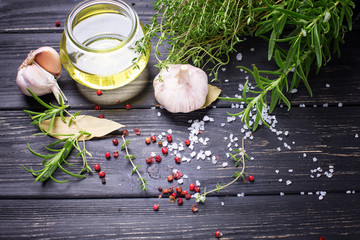 Bottle with olive oil with herb and spices ob black wooden background.