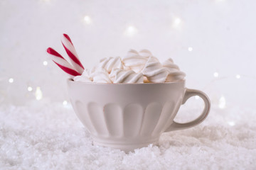 Obraz na płótnie Canvas Hot Coffee cup with marshmallows and red candy cane on a frosty winter background. Christmas holidays background. Copy space for text.