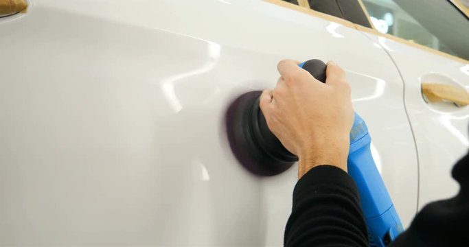 The professional guy (man) with headphones and a working uniform polishes the car body with a polishing tool. Concept from: Master class, Car Refreshment, Garage service, Special tools.