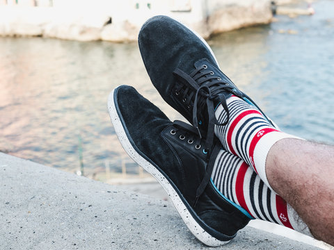 Men's legs in sports shoes and white socks with a bright, sea pattern in the shape of anchors on the background of a rocky shore on a summer, sunny day. Concept of fashion, sport and recreation - Powered by Adobe