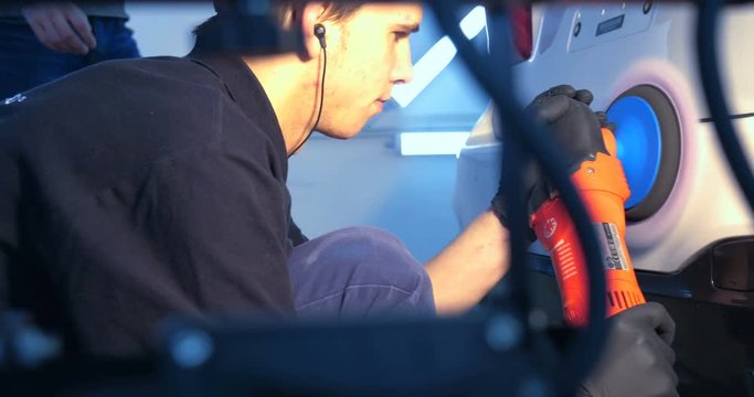 The professional guy (man) with headphones and a working uniform polishes the car body with a polishing tool. Concept from: Master class, Car Refreshment, Garage service, Special tools.