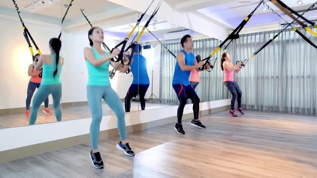 group of fitness people using trx straps jumping