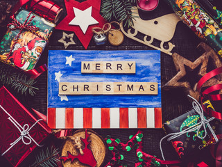 Greeting card with US Flag drawing, New Year and Christmas decorations, boxes with gifts on a brown surface. Top view, close-up, flat lay. Merry Christmas and Happy New Year