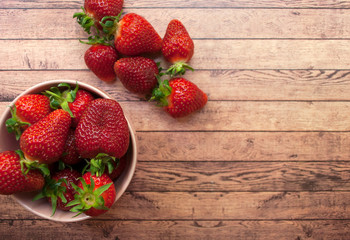 Flat lay of fresh strawberry in a pink bowl on wooden board. Healthy food concept.