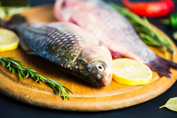fresh raw crucian fish with spices on wooden board on black background