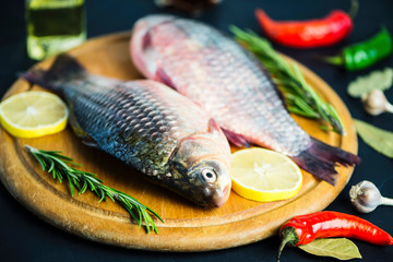 fresh raw crucian fish with spices on wooden board on black background