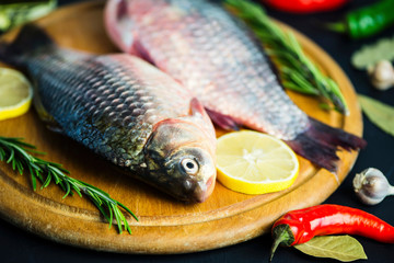 fresh raw crucian fish with spices on wooden board on black background