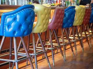 Blue, yellow, and red leather bar chairs lined up in front of bar counter