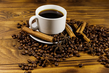Cup of coffee, roasted coffee beans, star anise and cinnamon sticks on wooden table
