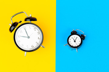 Black alarm clock on color block yellow and blue background