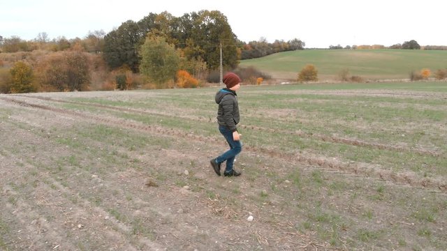 The lonely boy wanders in autumn in an empty, plowed, gray field. The croaker is looking for something in the field. The boy is running and walking.