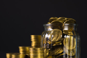 Coins stacks and gold coin money in the glass jar on dark background, for saving for the future banking finance concept.