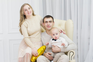 Husband, wife and one year old child are sitting in a leather chair. Portrait of a young family with a little son
