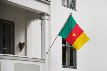 Cameroon flag hanging on a pole in front of the house. National flag waving on a home displaying on a pole on a front door of a building and raised at a full staff.