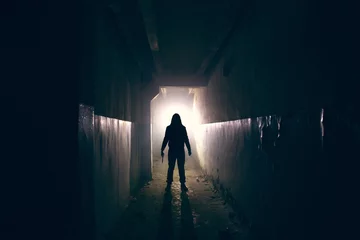 Fotobehang Silhouette of maniac with knife in hand in long dark creepy corridor, horror psycho maniac or serial killer concept © DedMityay
