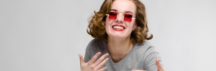 Charming young girl in a gray T-shirt on a gray background. Girl in red square-eyed glasses. The...