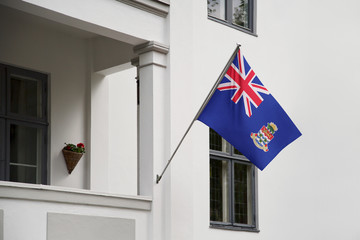Cayman Islands flag hanging on a pole in front of the house. National flag waving on a home displaying on a pole on a front door of a building and raised at a full staff.