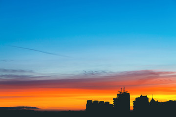 Cityscape with wonderful varicolored vivid dawn. Amazing dramatic multicolored cloudy sky above dark silhouettes of city buildings. Atmospheric background of sunrise. Orange sunlight. Copy space.