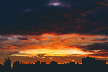 Obraz premium Cityscape with wonderful varicolored vivid fiery dawn. Amazing dramatic multicolored cloudy sky. Dark silhouettes of city buildings. Atmospheric background of sunrise in overcast weather. Copy space.