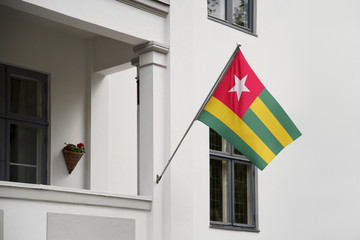 Togo flag hanging on a pole in front of the house. National flag waving on a home displaying on a pole on a front door of a building and raised at a full staff.