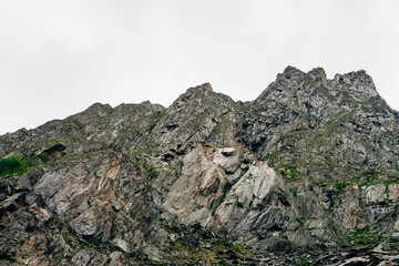 Giant ridge under cloudy sky. Misty rocky mountainside with vegetation. Amazing mountain range in overcast weather. Unusual foggy rocks. Atmospheric landscape of majestic nature of highlands.