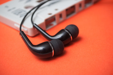 closeup of vintage audio cassette with black earphones on orange background