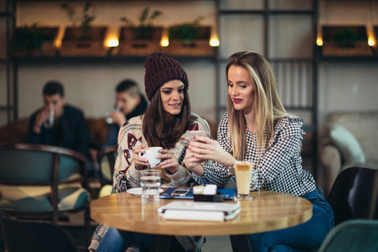 Two friends enjoying coffee together in a coffee shop and using phone
