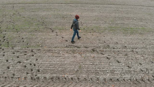 The lonely boy wanders in autumn in an empty, plowed, gray field. The croaker is looking for something in the field. The boy is running and walking.