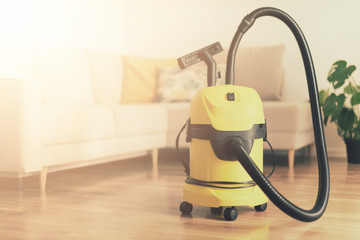 Yellow modern vacuum cleaner in living room. Copy space. Flat clean vacuuming concept. Green...