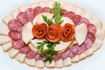 Different types delicacies of meat and cheese arranged in a plate over light background - selective focus