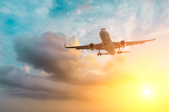 Commercial airplane flying above dramatic clouds during sunset