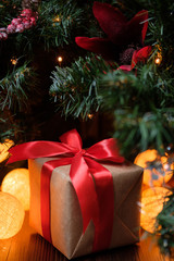 A gift in craft paper with a red ribbon on the background of a New Year's decorated Christmas tree with lights.