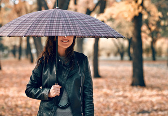 Woman under umbrella posing in autumn park. Bright yellow leaves and trees.