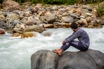 A person sitting on a rock in front of a river at Pahalgam in Kashmir