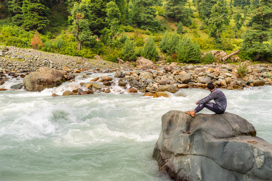 A person sitting on a rock in front of a river in Lidder Valley, at Pahalgam in Kashmir