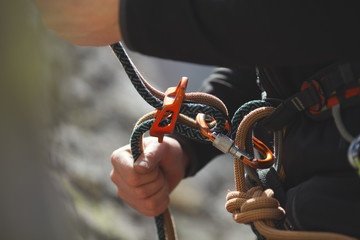 Easy belay-descender device in the hands of a climber closeup. Climbing gear and equipment. ...