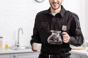 partial view of smiling policeman holding glass pot of filtered coffee at kitchen