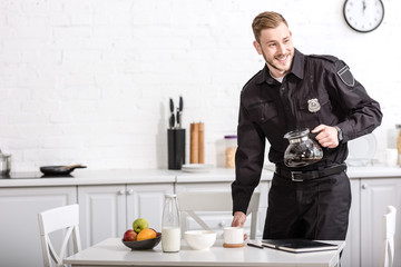 smiling handsome policeman holding glass pot of filtered coffee at breakfast time