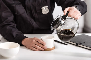 cropped view of policeman pouring filtered coffee from glass pot at kitchen table - Powered by Adobe