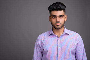 Young handsome Indian businessman against gray background
