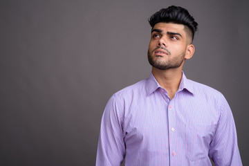 Young handsome Indian businessman against gray background