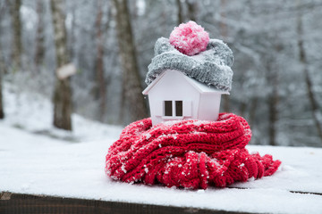 house in winter - heating system concept and cold snowy weather with model of a house wearing a knitted cap
