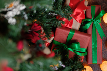 Gifts lie under the tree with a glowing gerland on a dark wooden floor