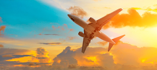 Airplane flying above dramatic clouds during sunset