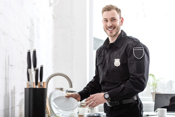 Handsome police officer washing dishes at kitchen