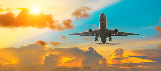 Commercial airplane flying above dramatic clouds during sunset