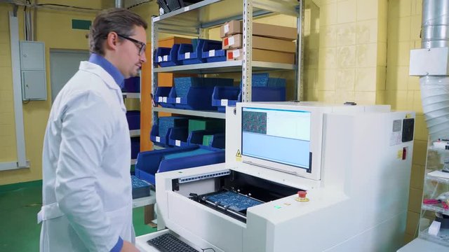 the worker puts the motherboard into the electrical Board inspection equipment. Printed circuit boards production factory. Technological process. Microchip production factory