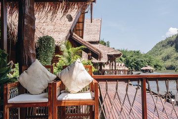 white pillows on wooden chair in thai raft floating house. The background is mountain and river.