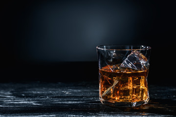Glass of whisky with ice on wooden table against dark background - obrazy, fototapety, plakaty