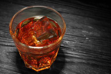 Glass of whisky with ice on wooden table, closeup